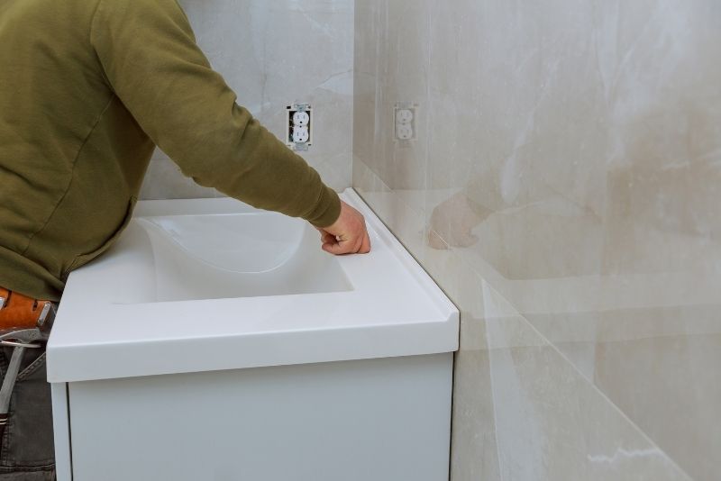 a man in a army green jacket leaning towards the bathroom sink