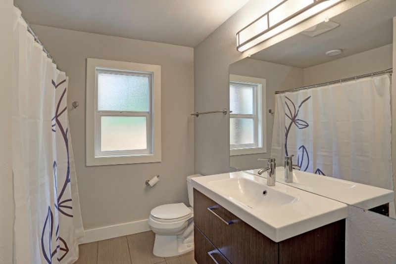 bathroom makeover picture with a window large mirror in front of the bathroon vanity facing a shower curtain