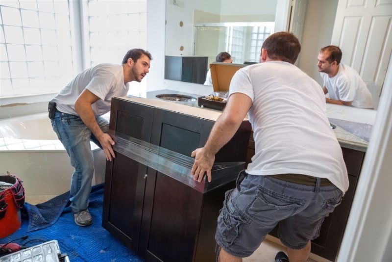 two mean in a white shirt moving the taped cabinet in dark brown colour towards the wall